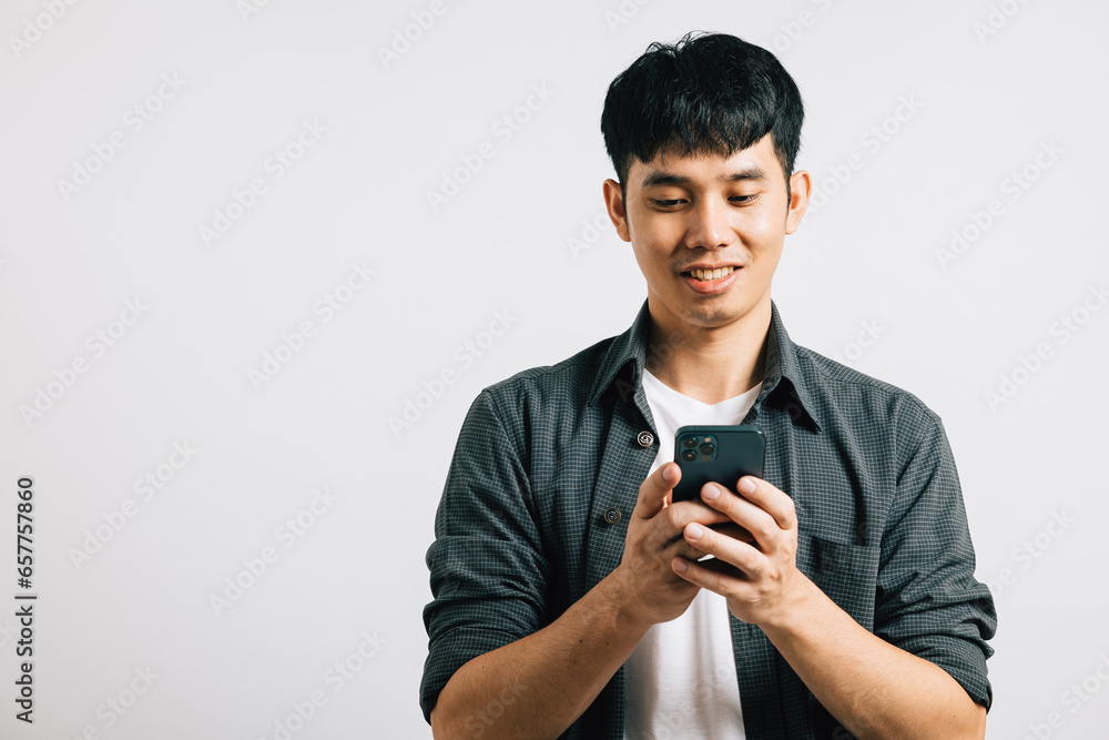 Portrait of a smiling Asian young man, excited while typing a text message on his smart mobile phone for online communication. Studio shot isolated on white, showcasing his enthusiasm for technology. Portrait of a smiling Asian young man, excited while typing a text message on his smart mobile phone for online communication. Studio shot isolated on white, showcasing his enthusiasm for technology.