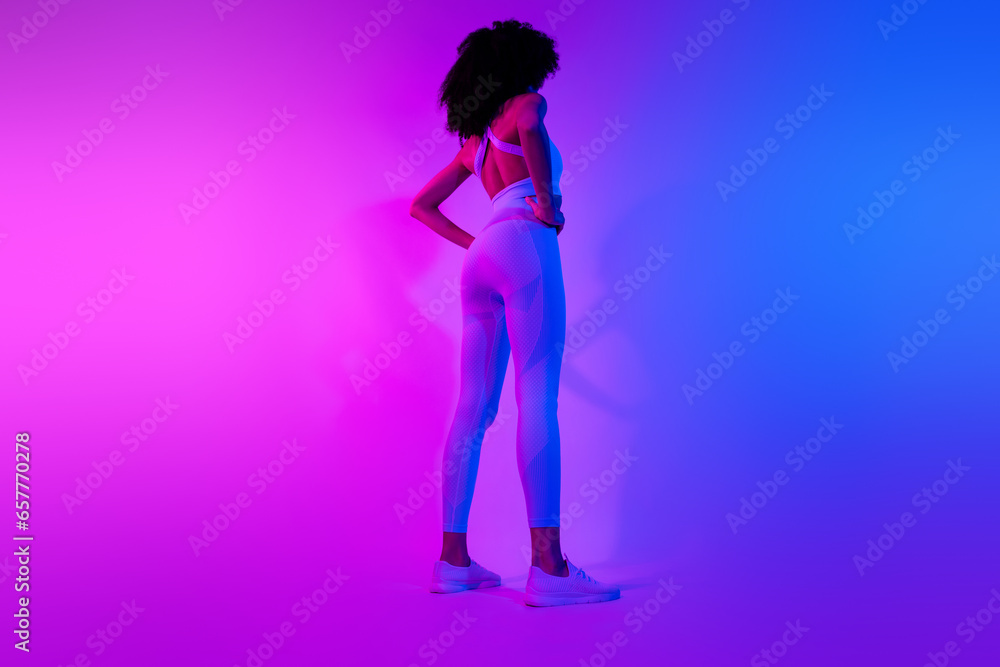 Rear back cadre of stylish sportswear girl professional athlete big muscles booty ass isolated on blue pink neon filter background Rear back cadre of stylish sportswear girl professional athlete big muscles booty ass isolated on blue pink neon filter background