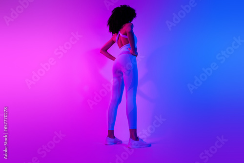 Rear back cadre of stylish sportswear girl professional athlete big muscles booty ass isolated on blue pink neon filter background
