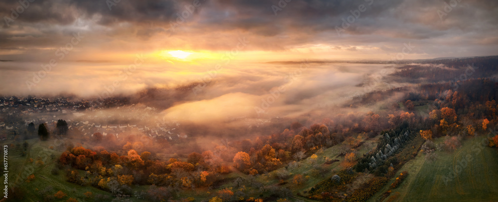 Highly dramatic sunrise scenery from above the fog. Panoramic aerial view of a beautiful landscape with magnificent red light illuminating dark clouds and the mist