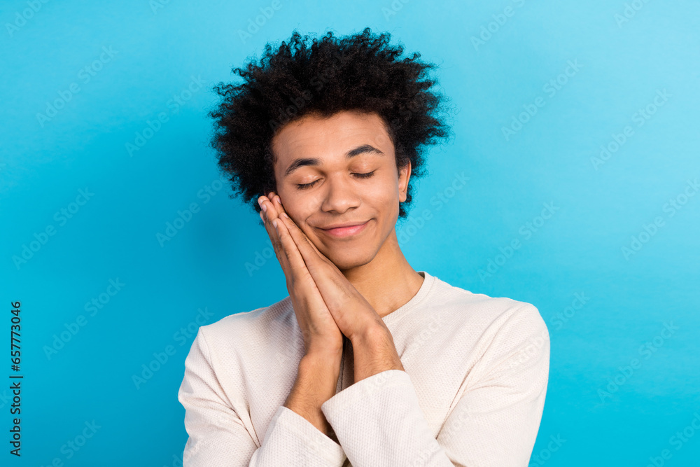 Photo portrait of nice young guy hands together closed eyes sleeping wear trendy white pajama outfit isolated on blue color background Photo portrait of nice young guy hands together closed eyes sleeping wear trendy white pajama outfit isolated on blue color background