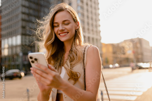 woman walking in sunny city street with phone