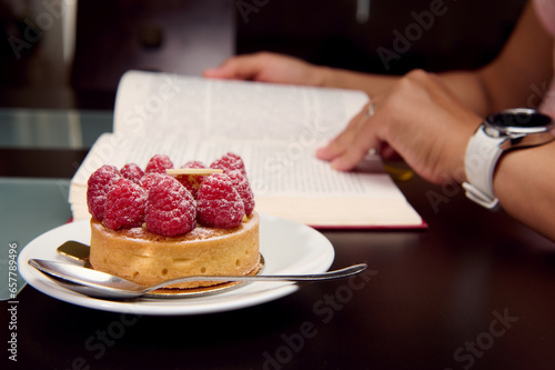 A raspberry tartlet over the background of a woman reading book