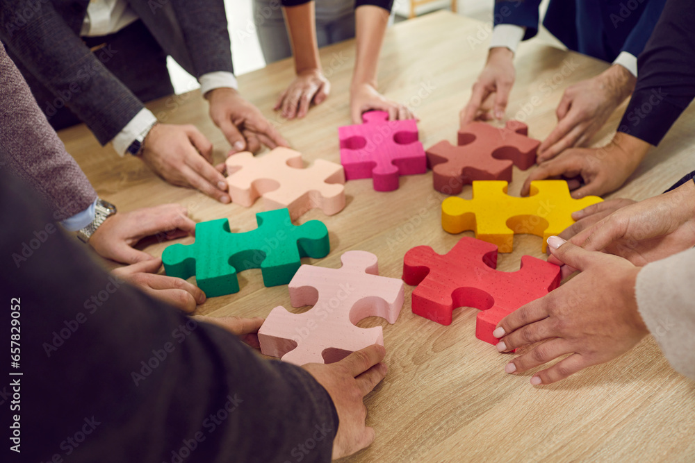 Cropped hands of a group of business people assembling big multicolor puzzle. Cooperation, teamwork, help and support concept. coworkers join jigsaw pieces in the office. Top view. Cropped hands of a group of business people assembling big multicolor puzzle. Cooperation, teamwork, help and support concept. coworkers join jigsaw pieces in the office. Top view.