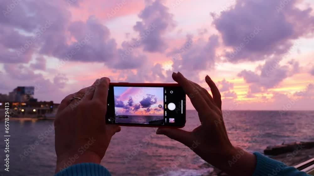 Woman's hands holding smartphone and shooting sunset sky over the sea Woman's hands holding smartphone and shooting sunset sky over the sea