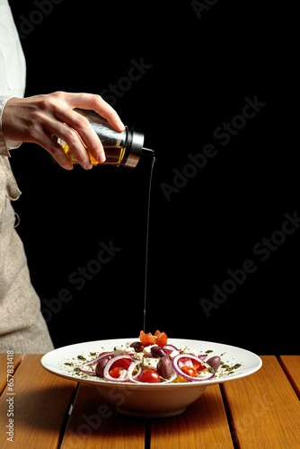 view of a waitress's hand dressing a salad on the table, black background, 