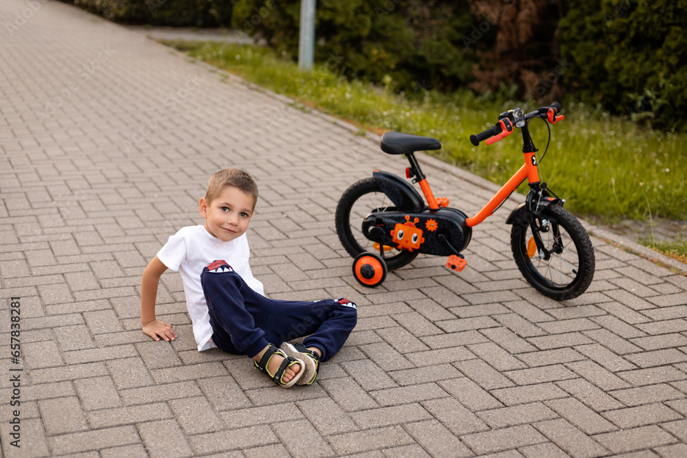 A boy sits on the ground near a bicycle. A schoolboy rides a bicycle A boy sits on the ground near a bicycle. A schoolboy rides a bicycle