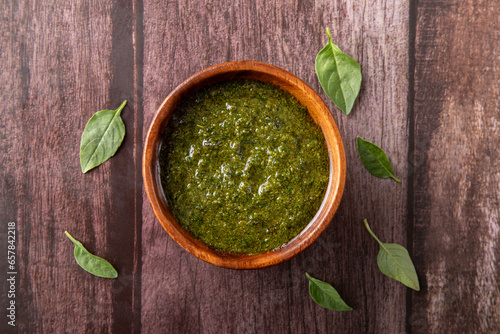 Pesto sauce on wooden bowl. Rustic background. Basil leafs on wooden background.