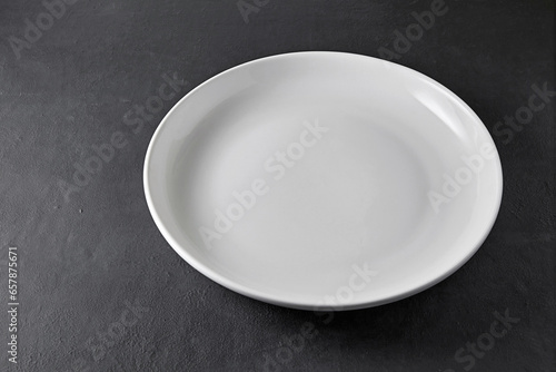 White ceramic plate on a black stone table. Empty plate to display food in restaurant menu