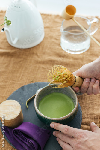 Traditional Japanese green tea match close-up. Matcha tea ceremony, a bamboo Chassen whisk for whipping and tea in a bowl on the brown background.