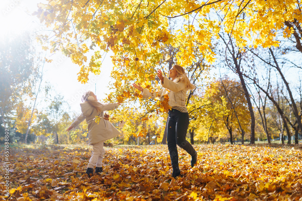 Hello Autumn. Smiling young mother and daughter having fun in an autumn park with yellow leaves. Family enjoying a walk and spending time together. Hello Autumn. Smiling young mother and daughter having fun in an autumn park with yellow leaves. Family enjoying a walk and spending time together.