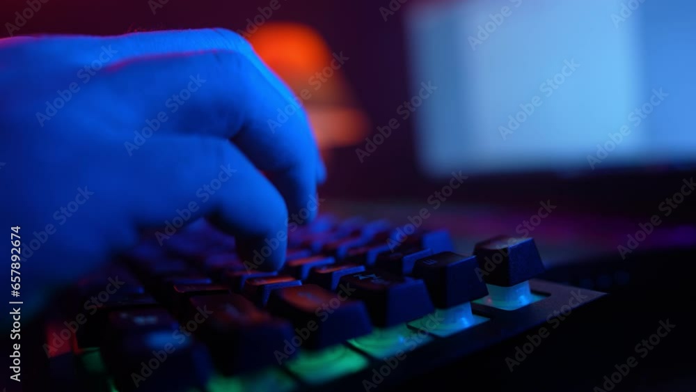 Close-up, Unrecognizable Man Using a Computer Keyboard to Code a Website in Neon Lighting. Hacker and Cybercrime or Cyberspace Concept. Close-up, Unrecognizable Man Using a Computer Keyboard to Code a Website in Neon Lighting. Hacker and Cybercrime or Cyberspace Concept.