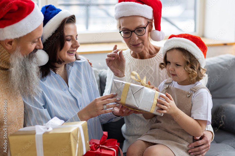 Fototapeta premium Grandmother, grandfather, daughter and granddaughter celebrating holidays at home together. Happy smiling family near beautiful Christmas new year tree exchanging gifts in the morning