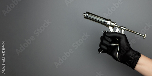 Veterinary injection syringe or vaccination gun in hand in black nitrile glove, banner with copy space. Vet concept photo