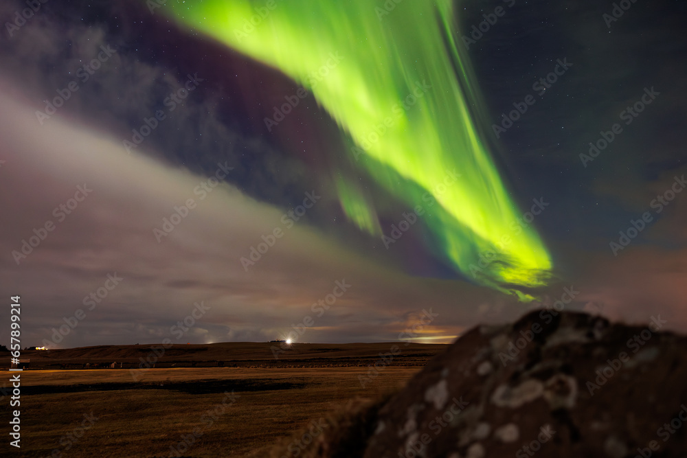 At sundown in Iceland, aurora borealis brightens up night sky in outstanding hues of green and violet, forming magical icelandic landscape. Stars sparkle around northern lights.