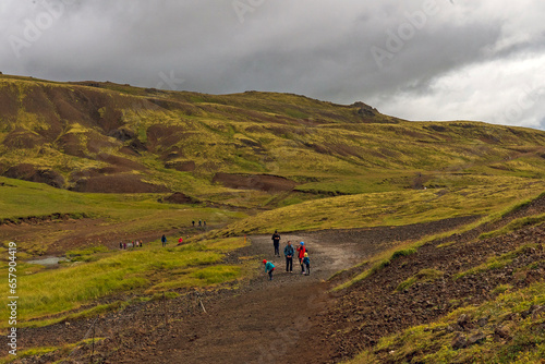 Tourists hike through mossy and wetland terrain of Reykjadalur Valley, Iceland. Valley is known for its mudpots, soda springs and geothermal activity.