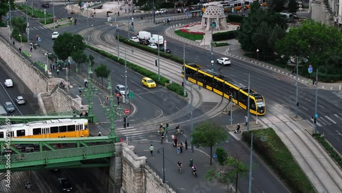 Aerial view of traffic in city. Cars and trams crossing intersection in city. Pedestrians and cyclists crossing road. Budapest, Hungary