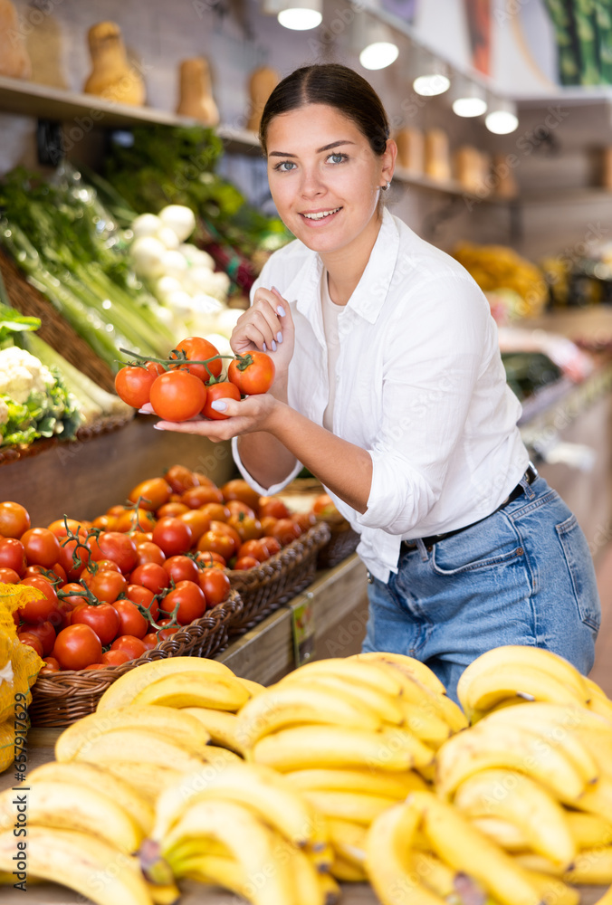 Obraz premium Portrait of positive satisfied girl buying fresh tomatoes in grocery shop