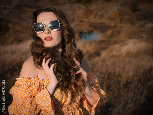 young brunette in sunglasses against the backdrop of a natural autumn landscape close-up
