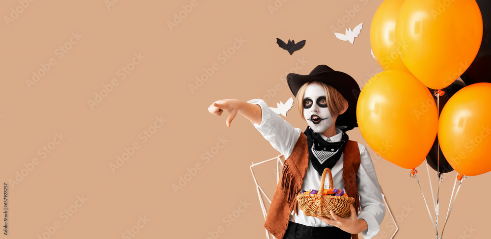 Little boy in Halloween costume and with candies on beige background with space for text