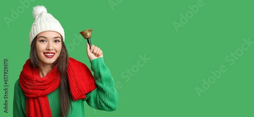 Beautiful young Asian woman with jingle bell on green background with space for text photo