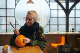 A modern blonde woman in military uniform is carving spooky pumpkins with a knife for Halloween night