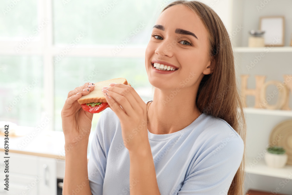 Beautiful young woman eating tasty sandwich in kitchen, closeup Beautiful young woman eating tasty sandwich in kitchen, closeup