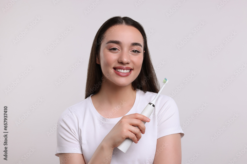 Happy young woman holding electric toothbrush on white background Happy young woman holding electric toothbrush on white background