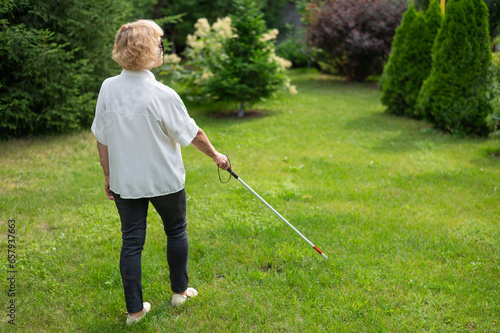 Rear view of an elderly blind woman walking in the park with a tactile cane. 