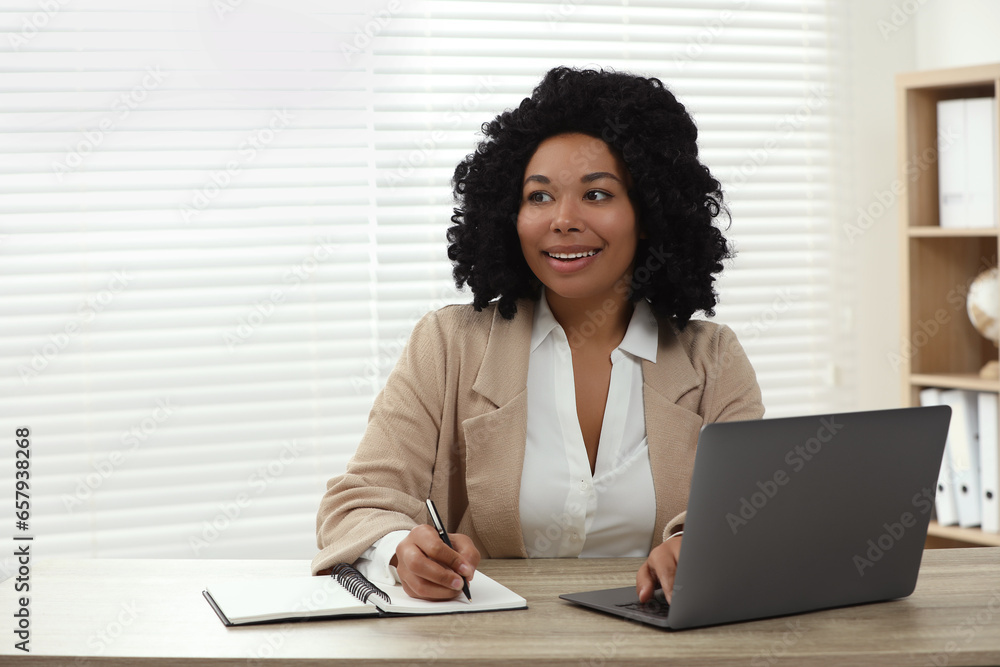 Happy woman writing notes and using laptop at wooden desk indoors. Space for text Happy woman writing notes and using laptop at wooden desk indoors. Space for text