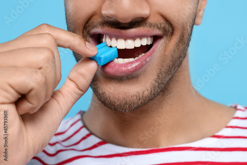 Happy man with bubble gum on light blue background, closeup