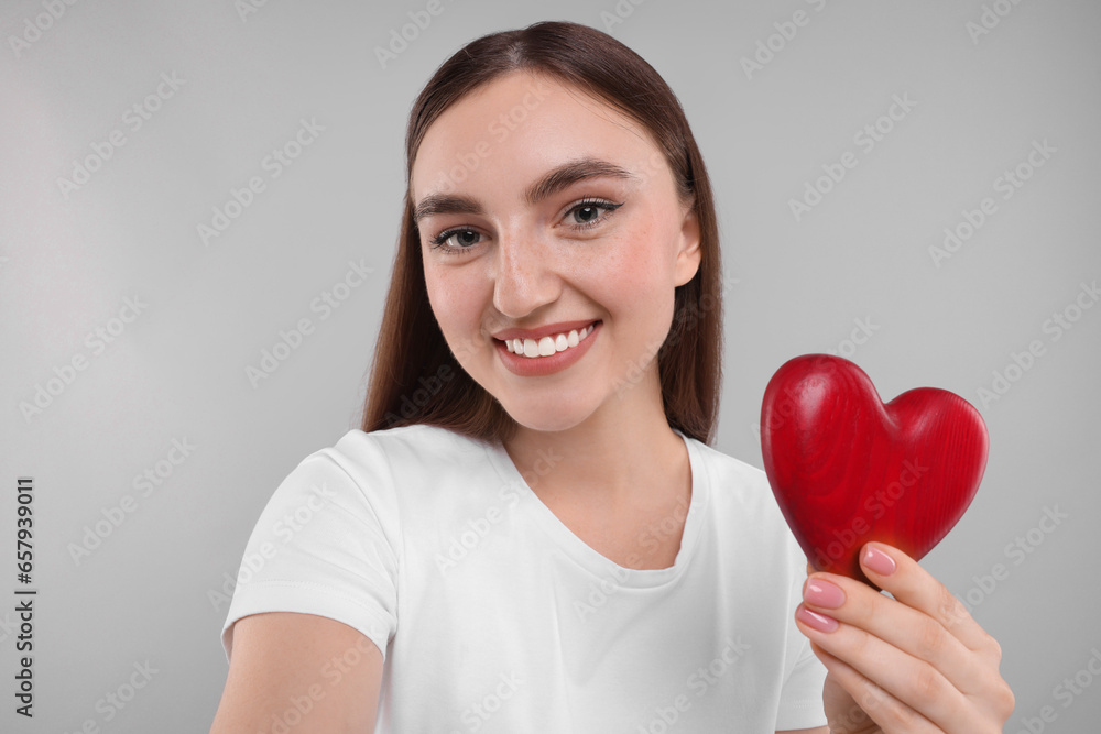 Smiling woman holding red heart on light grey background Smiling woman holding red heart on light grey background