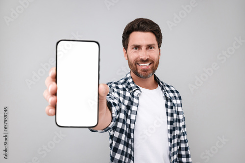Handsome man showing smartphone in hand on light grey background