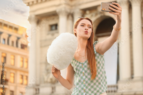 Woman with cotton candy taking selfie on city street. Space for text