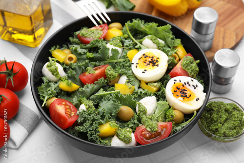 Delicious salad with pesto sauce in bowl and ingredients on white tiled table, closeup
