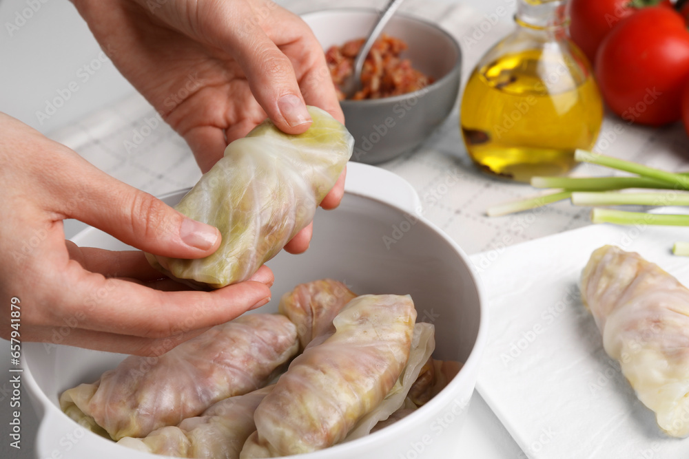 Woman putting uncooked stuffed cabbage roll into ceramic pot at table, closeup