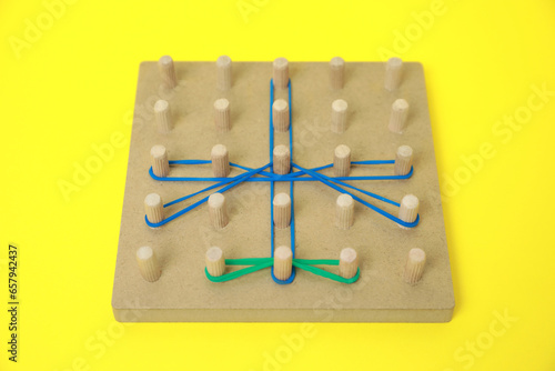 Wooden geoboard with dragonfly shape made of rubber bands on yellow background. Educational toy for motor skills development photo