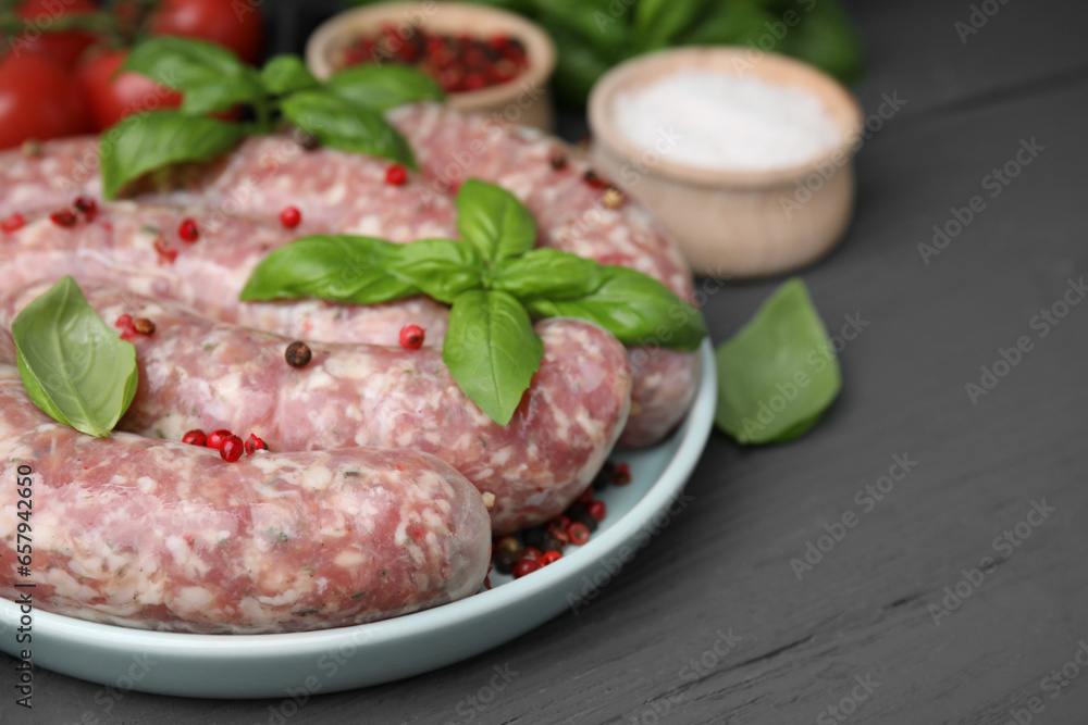 Raw homemade sausages, basil leaves and peppercorns on grey wooden table, closeup