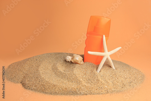 Sand with bottle of sunscreen, starfish and seashells against orange background. Sun protection