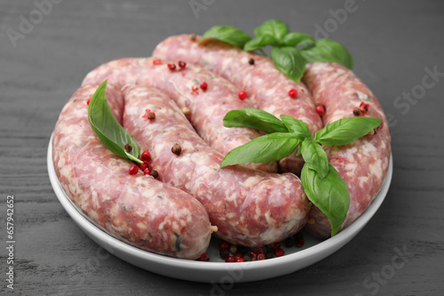 Raw homemade sausages, basil leaves and peppercorns on grey wooden table, closeup