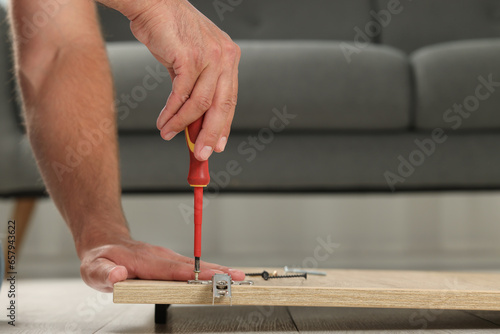 Man with screwdriver assembling furniture on floor indoors, closeup. Space for text