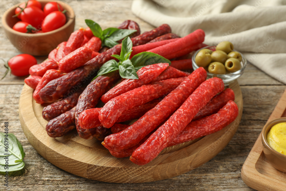 Different thin dry smoked sausages, basil and olives on wooden table, closeup