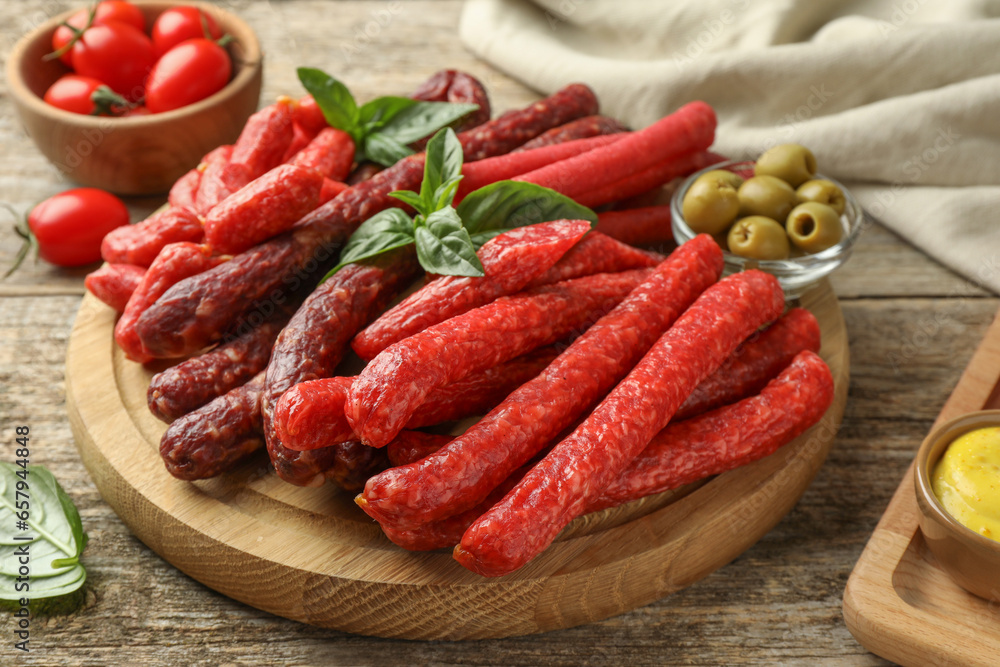 Different thin dry smoked sausages, basil and olives on wooden table, closeup Different thin dry smoked sausages, basil and olives on wooden table, closeup