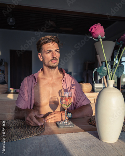 a man with a glass of water sits at a table with a vase of flowers