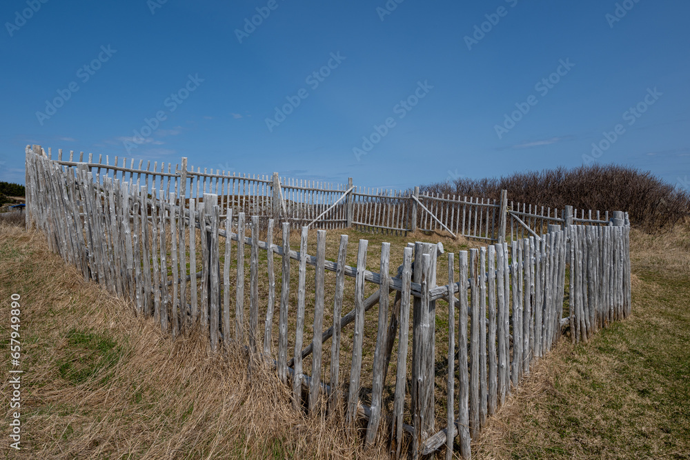 A rustic old-fashioned cattle corral made of logs. The weathered fence and gate are in a square pen pattern. There's hay or straw growing around the vintage animal enclosure on the farmland.