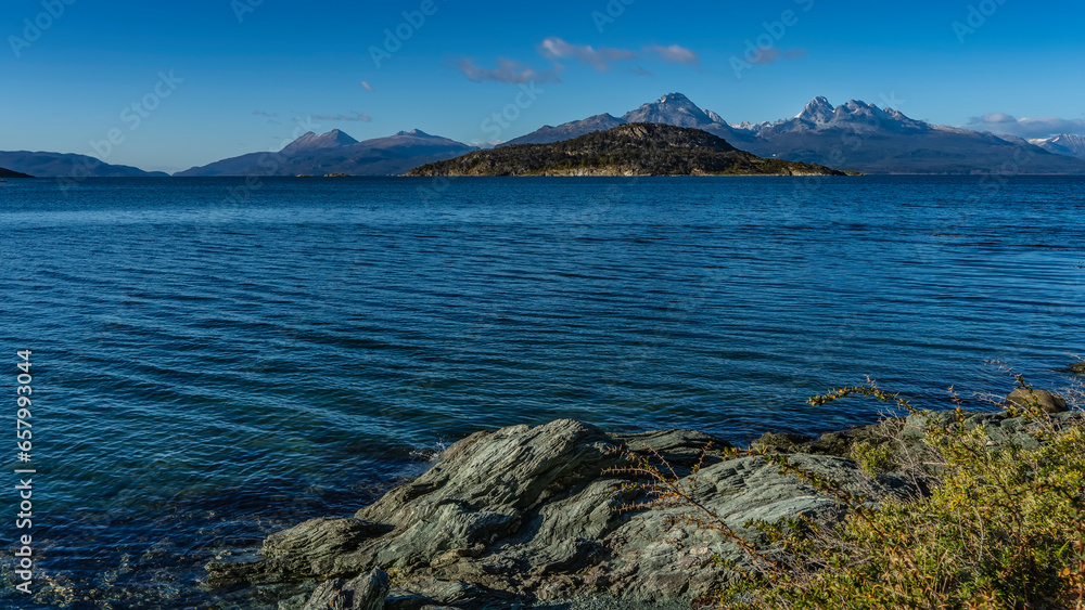 A beautiful blue lake with rocky shores. Ripples on the water. Beautiful mountains against the azure sky and clouds in the distance. Argentina. Ensenada Bay. Tierra del Fuego National Park. Ushuaia