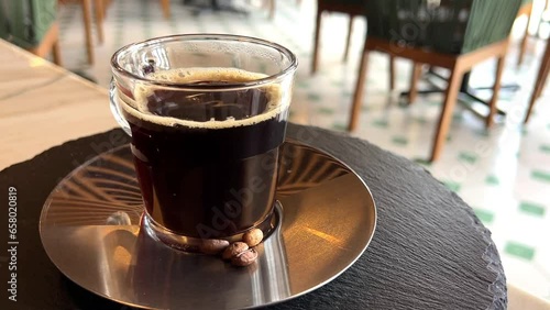 American coffee in a glass cup on a polished steel plate and coffee beans to decorate rotating to show their exquisiteness