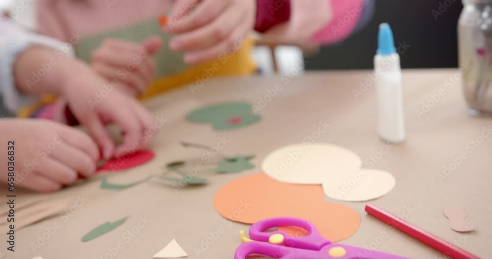 Happy biracial mother and daughter sticking colourful cutouts in sunny living room Happy biracial mother and daughter sticking colourful cutouts in sunny living room