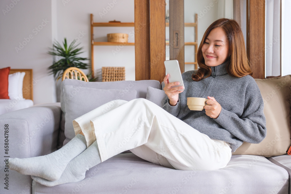 Portrait image of a beautiful young woman holding coffee cup and using smart phone at home Portrait image of a beautiful young woman holding coffee cup and using smart phone at home