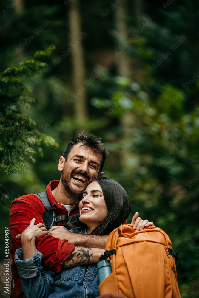 A multi-ethnic couple pauses on a tree log, catching their breath and savoring the tranquility of the mountain woods during their hike A multi-ethnic couple pauses on a tree log, catching their breath and savoring the tranquility of the mountain woods during their hike